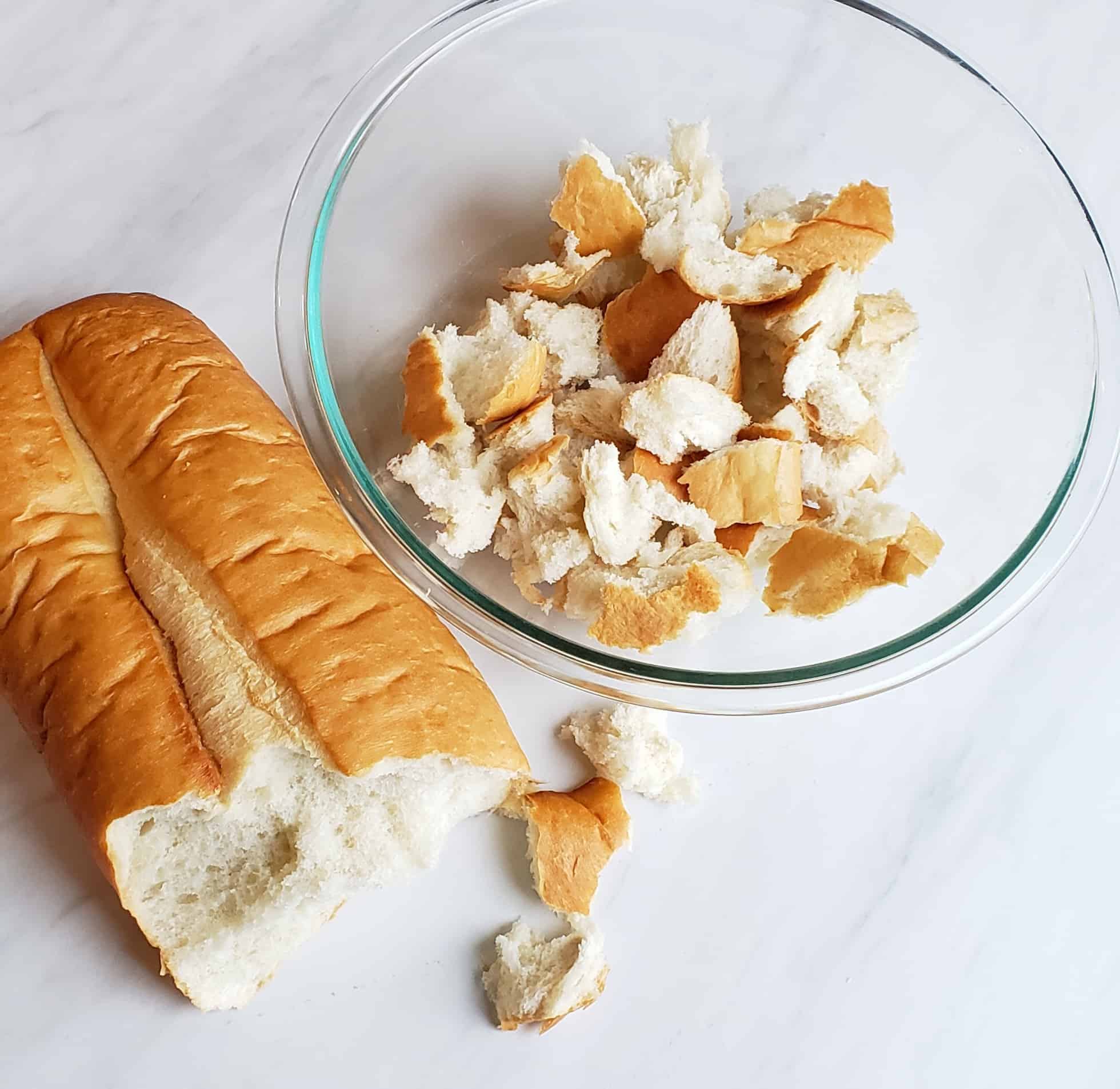 loaf of french bread being torn in a clear glass bowl