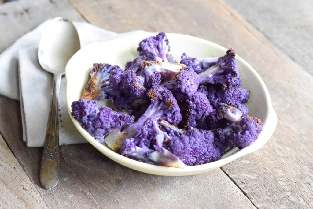 Roasted Purple Cauliflower in a white bowl on light wooden surface