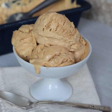 scoops of dulce de leche ice cream in a small pedastle bowl on antique linen