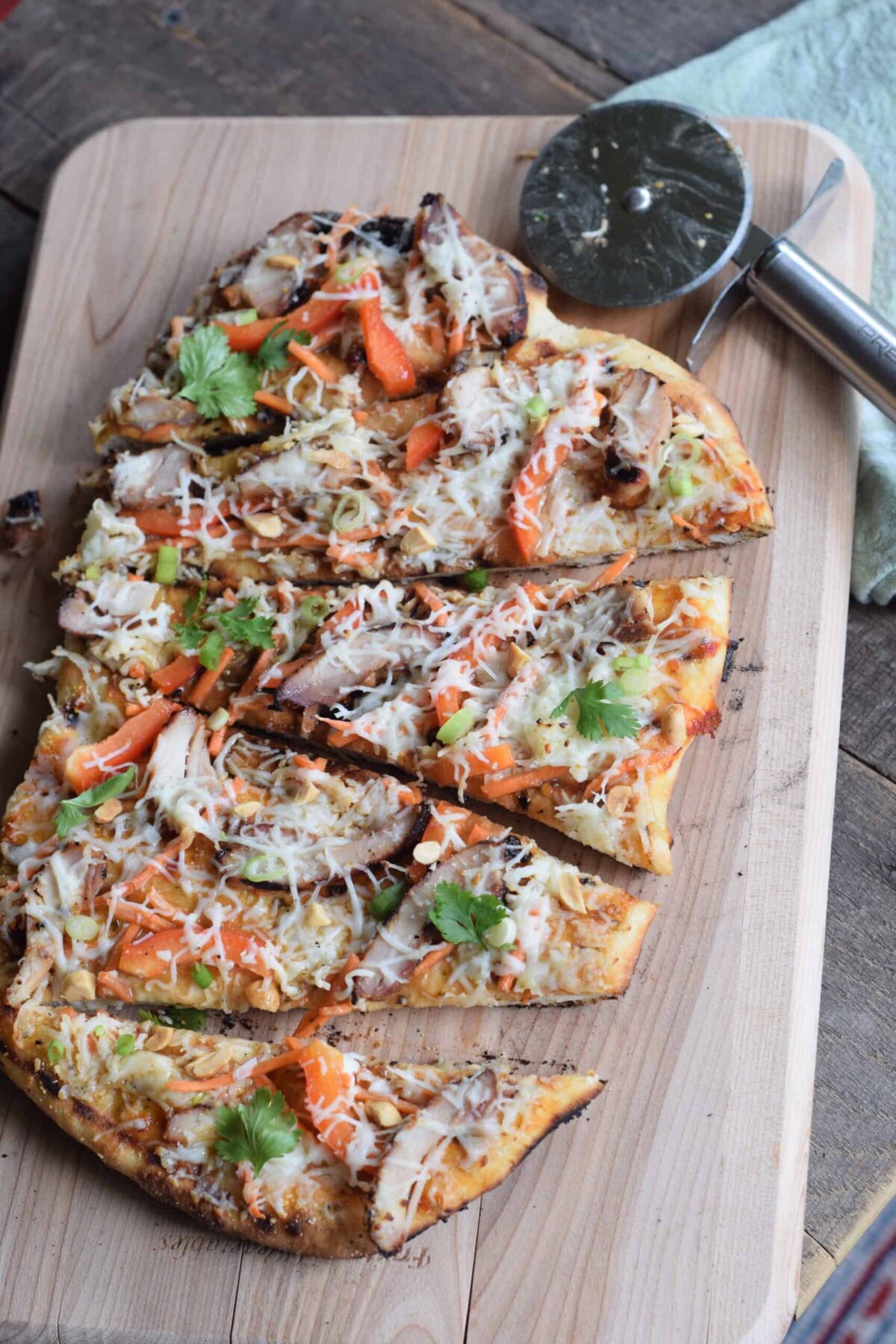 Thai Chicken Grilled Pizza made with Naan bread. pizza wheel on wooden cutting board