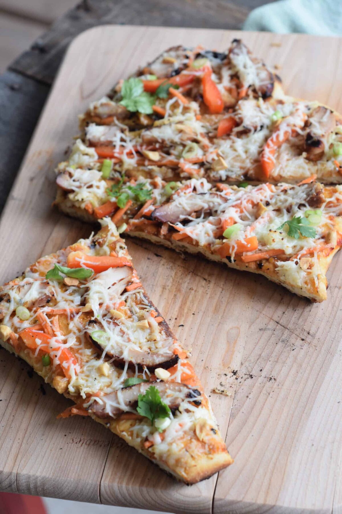 Thai Grilled Chicken Pizza made with Naan bread on wooden cutting board with slice cut off