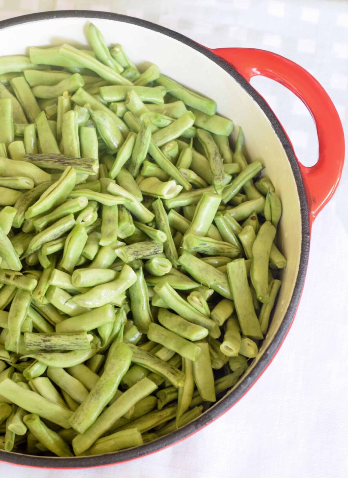 Uncooked fresh green beans snapped in an enamel red cast iron pot