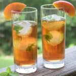 two tall glasses of tea over round mint ice cubes and garnished with peach slices