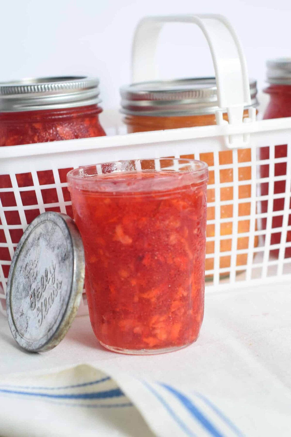 Easy Freezer strawberry jam by a white plastic basic and antique lid propped on the jar