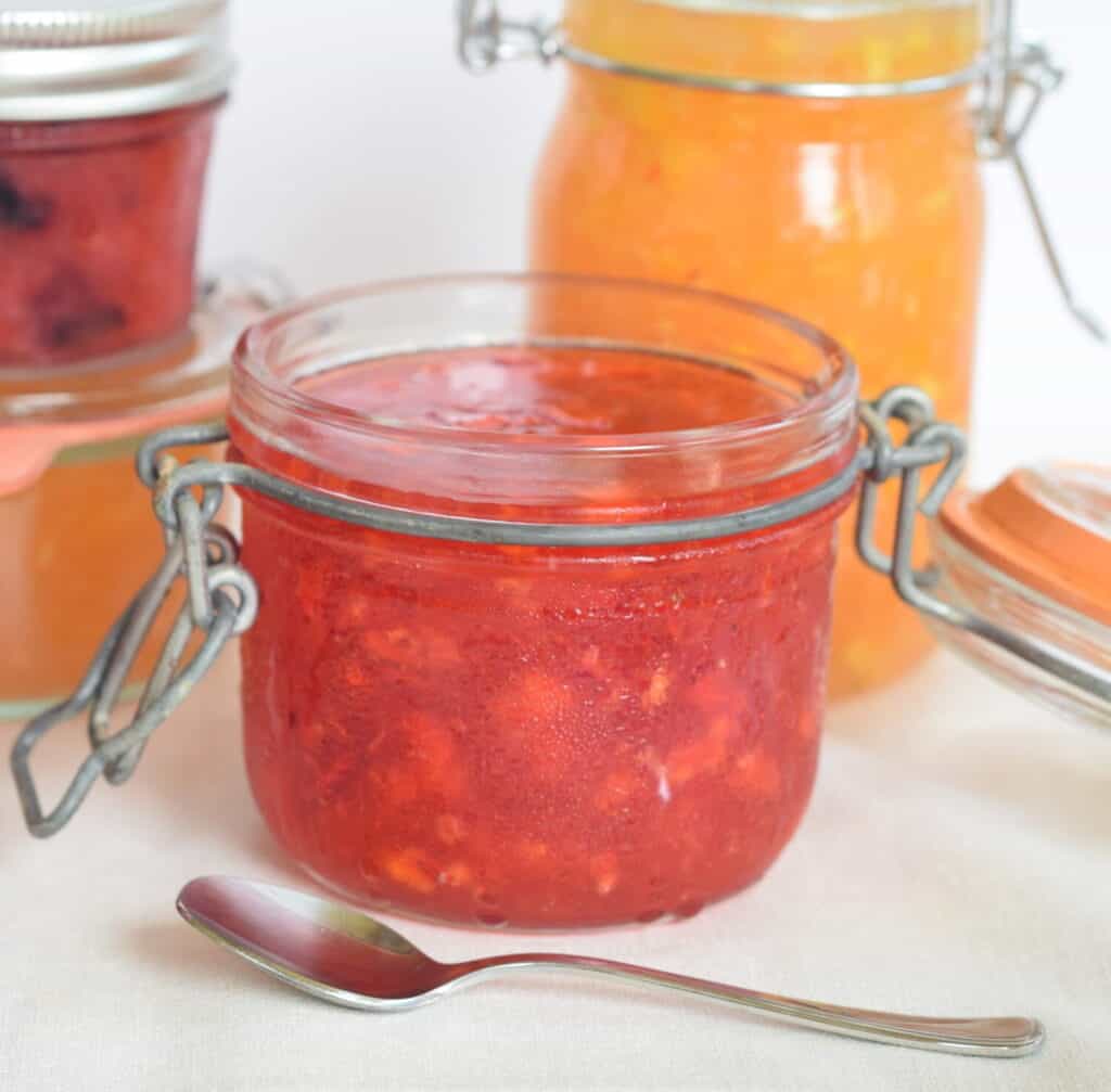 strawberry freezer jam in old fashioned clamp jar with peach and strawberry-blueberry jam in the background