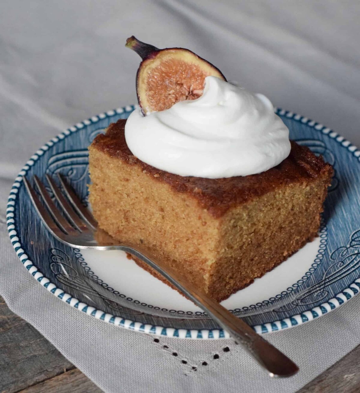 Fig Jam Cake with dollop whipped cream and fig half on a blue plate and fork