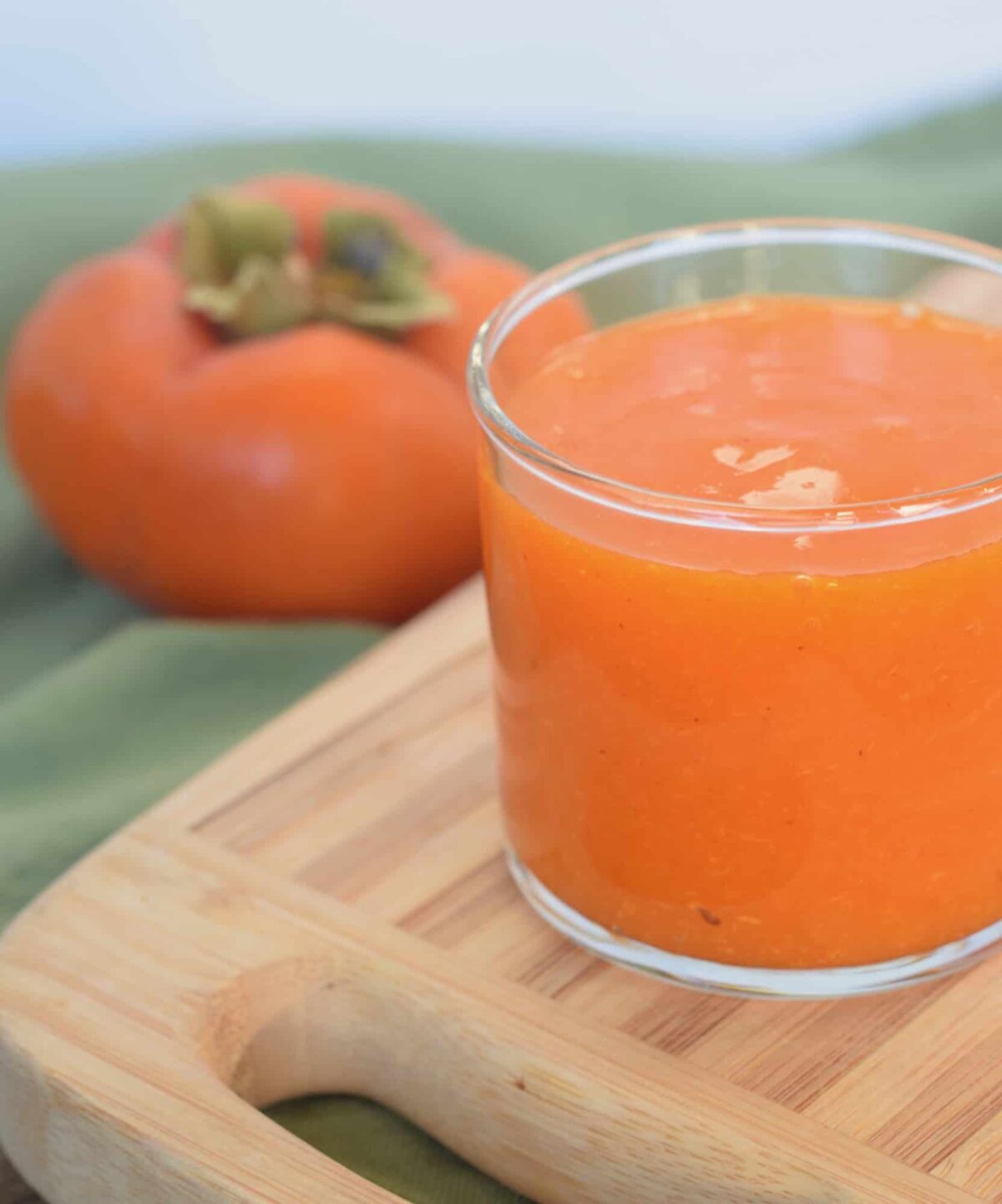 Bright orange persimmon pulp in a glass cup with a persimmon in the background