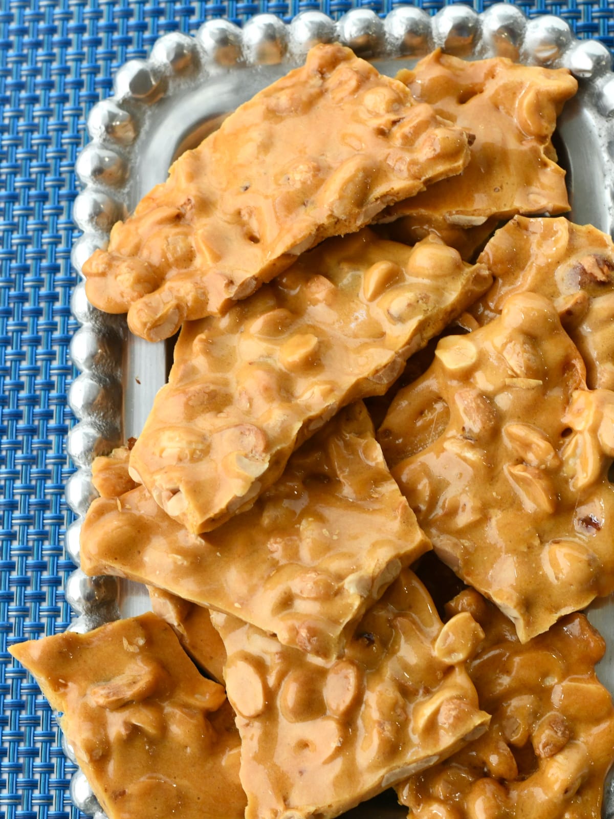 Large pieces of peanut brittle on a silver platter.