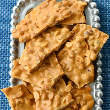 Pieces of peanut brittle on a pewter rectangle platter.