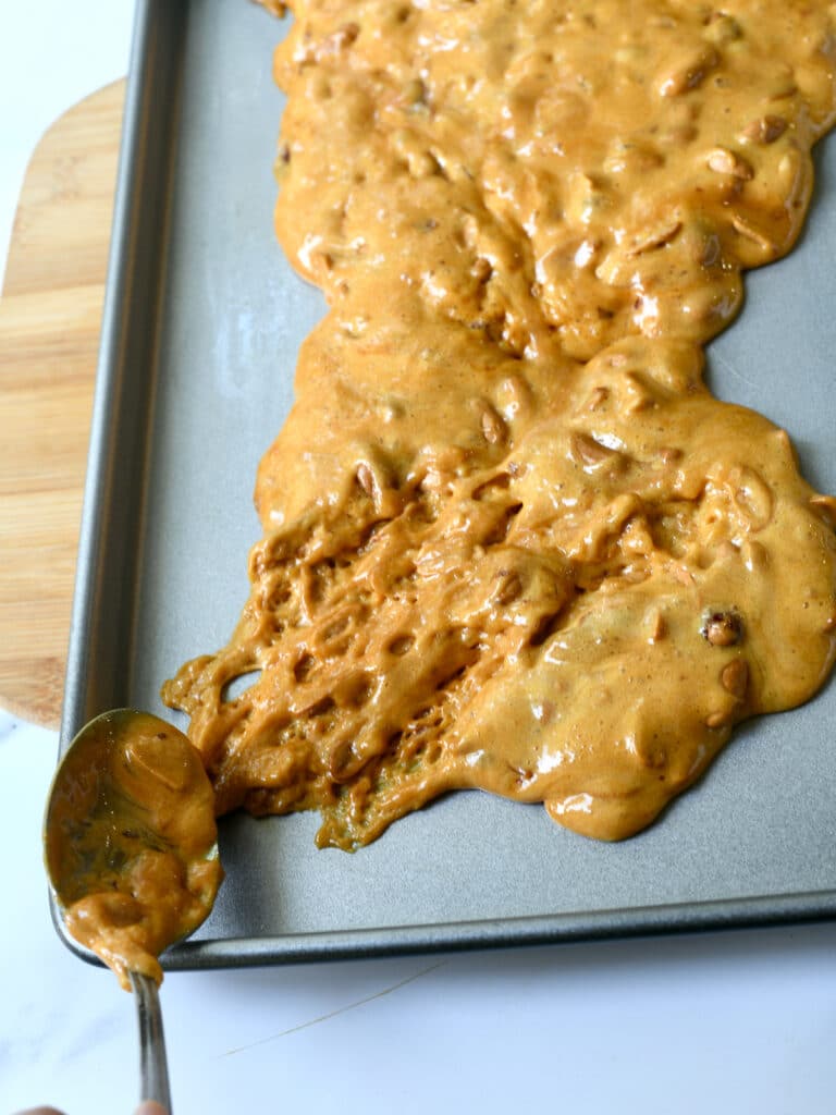 Metal spoon spread hot peanut brittle on baking sheet.
