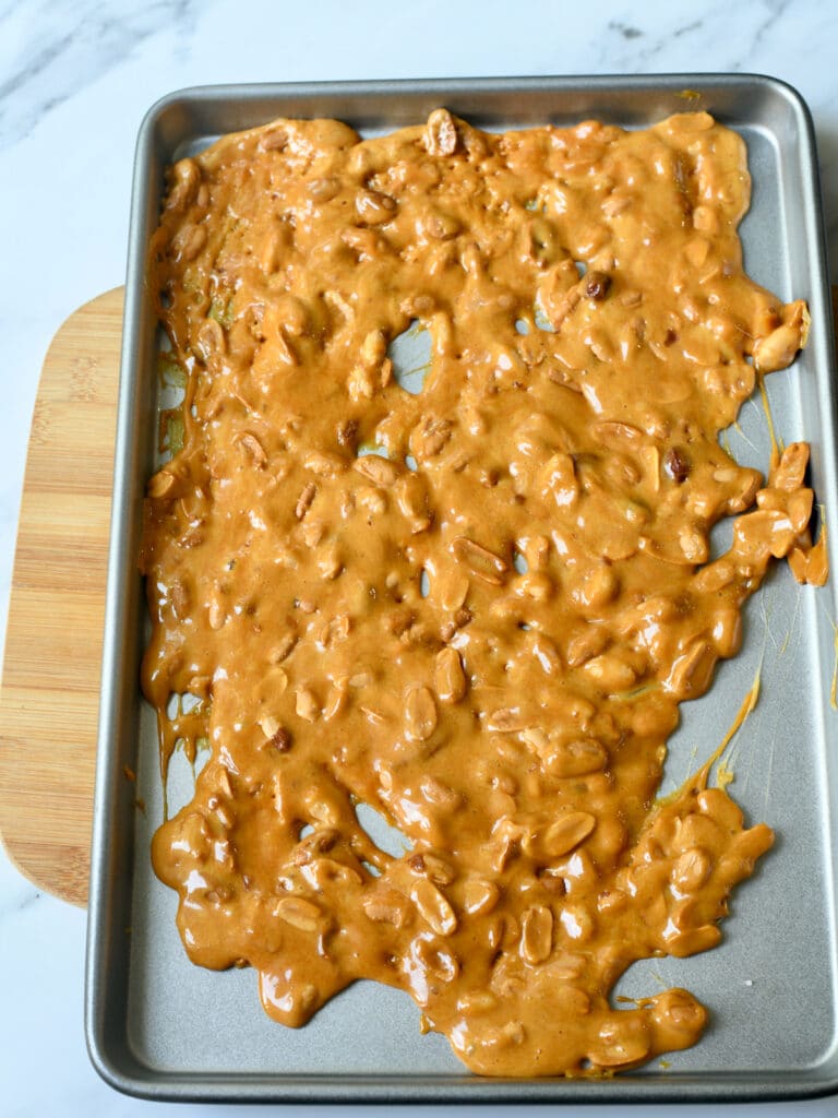 Peanut brittle cooling on baking sheet on cutting board.
