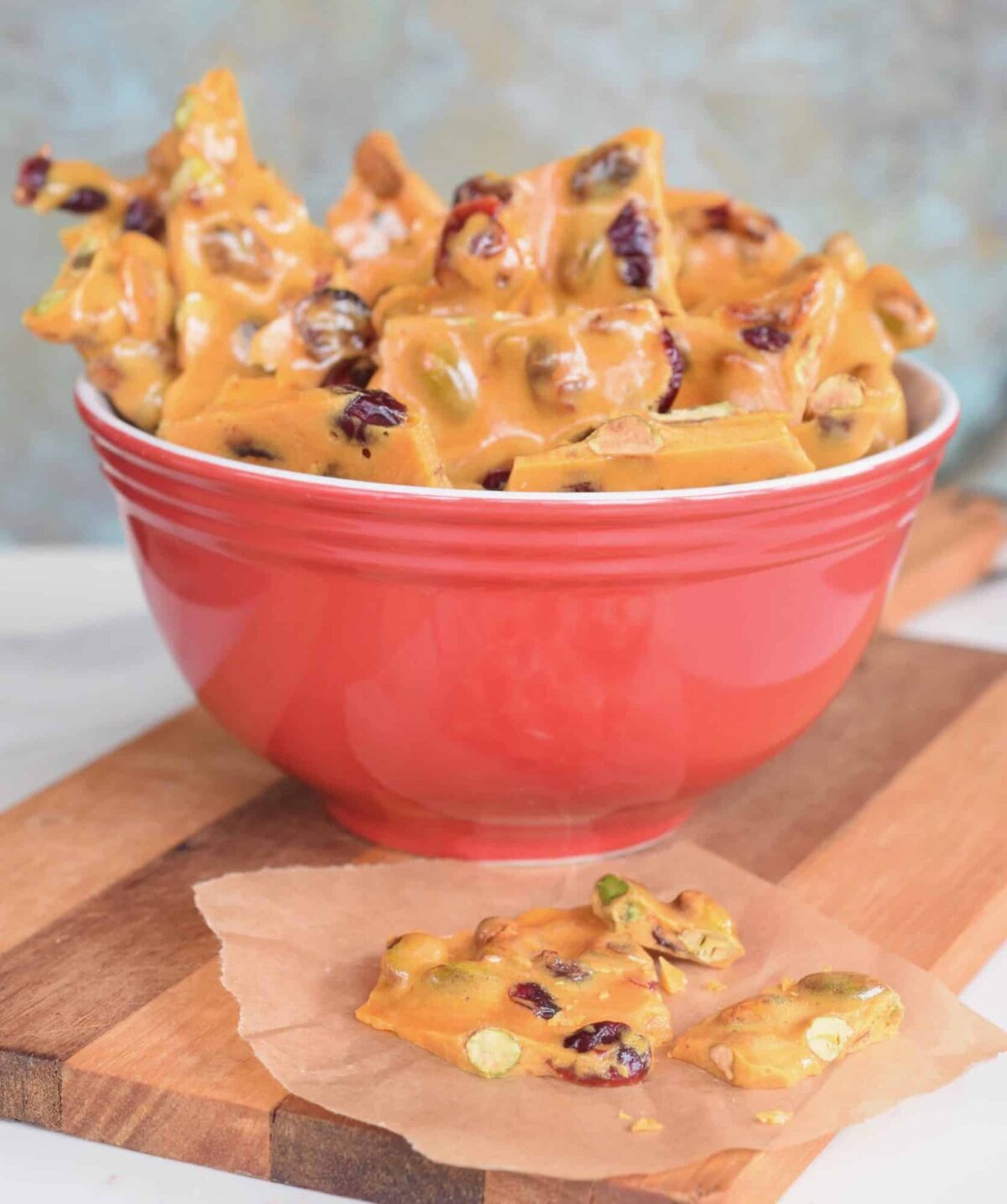 Cranberry Pistachio Brittle in a red bowl. one broken piece on brown parchment