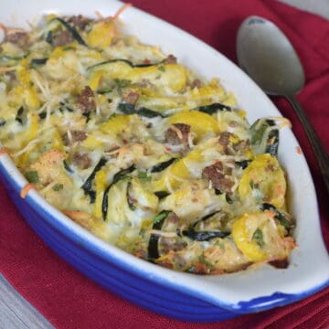 sausage, yellow and zucchini squash casserole in a blue oblong dish on red napkin and antique spoon