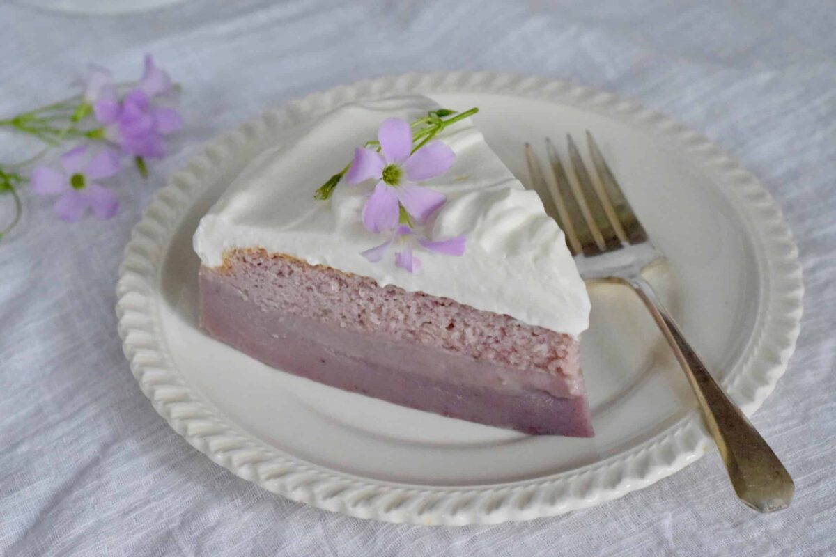 purple sweet potato magic cake slice on a white plate garnished with purple oxalis flower