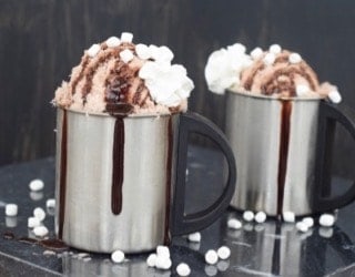 Two silver mugs of chocolate snow ice cream with chocolate drizzle coming down the side.