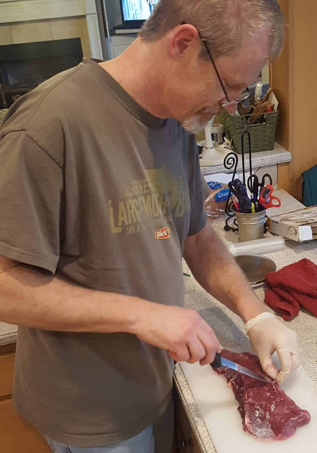 Man in t shirt cutting of silver skin on deer meat