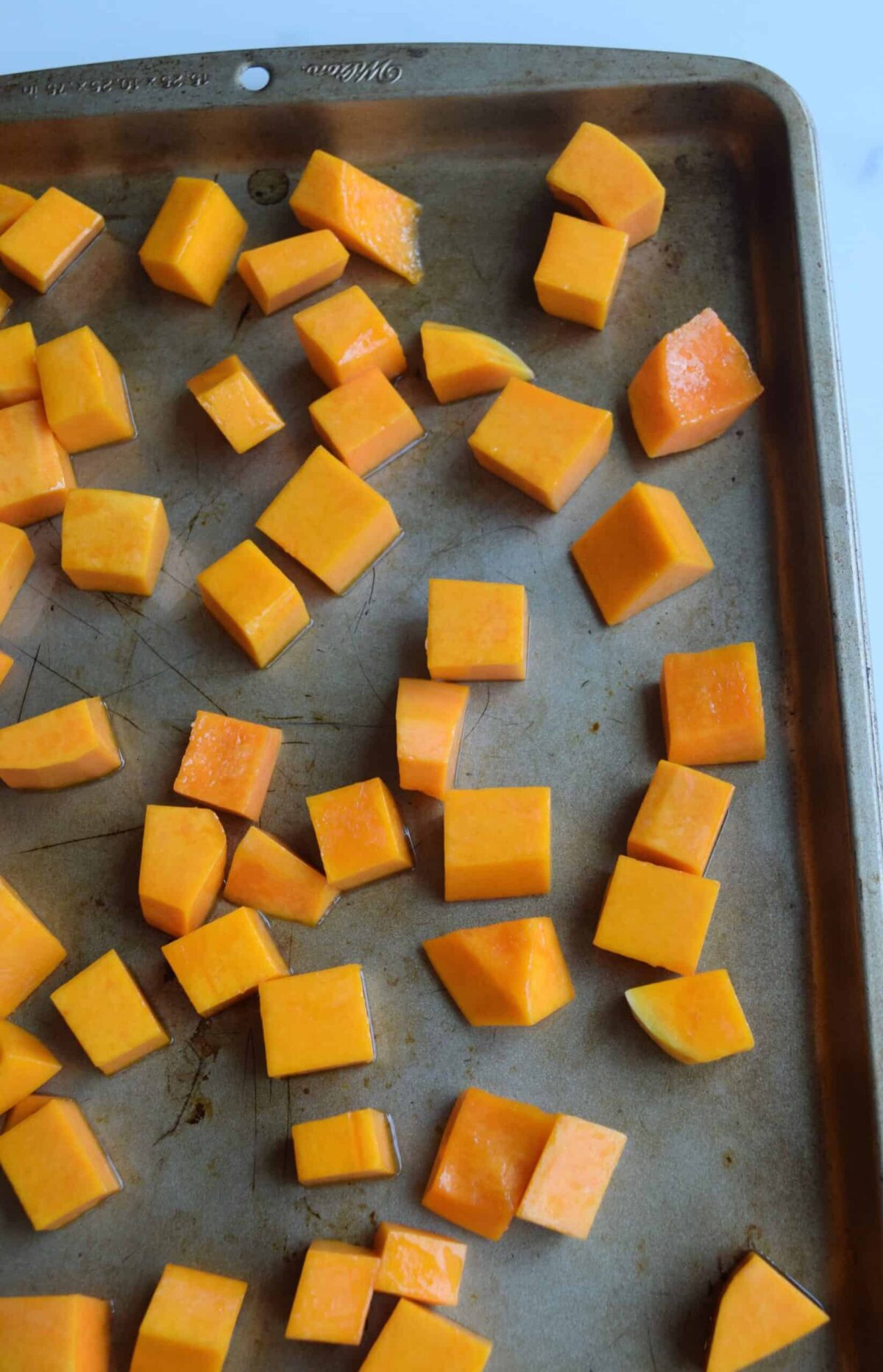 Baking sheet pan with butternut squash in single layer before baking.