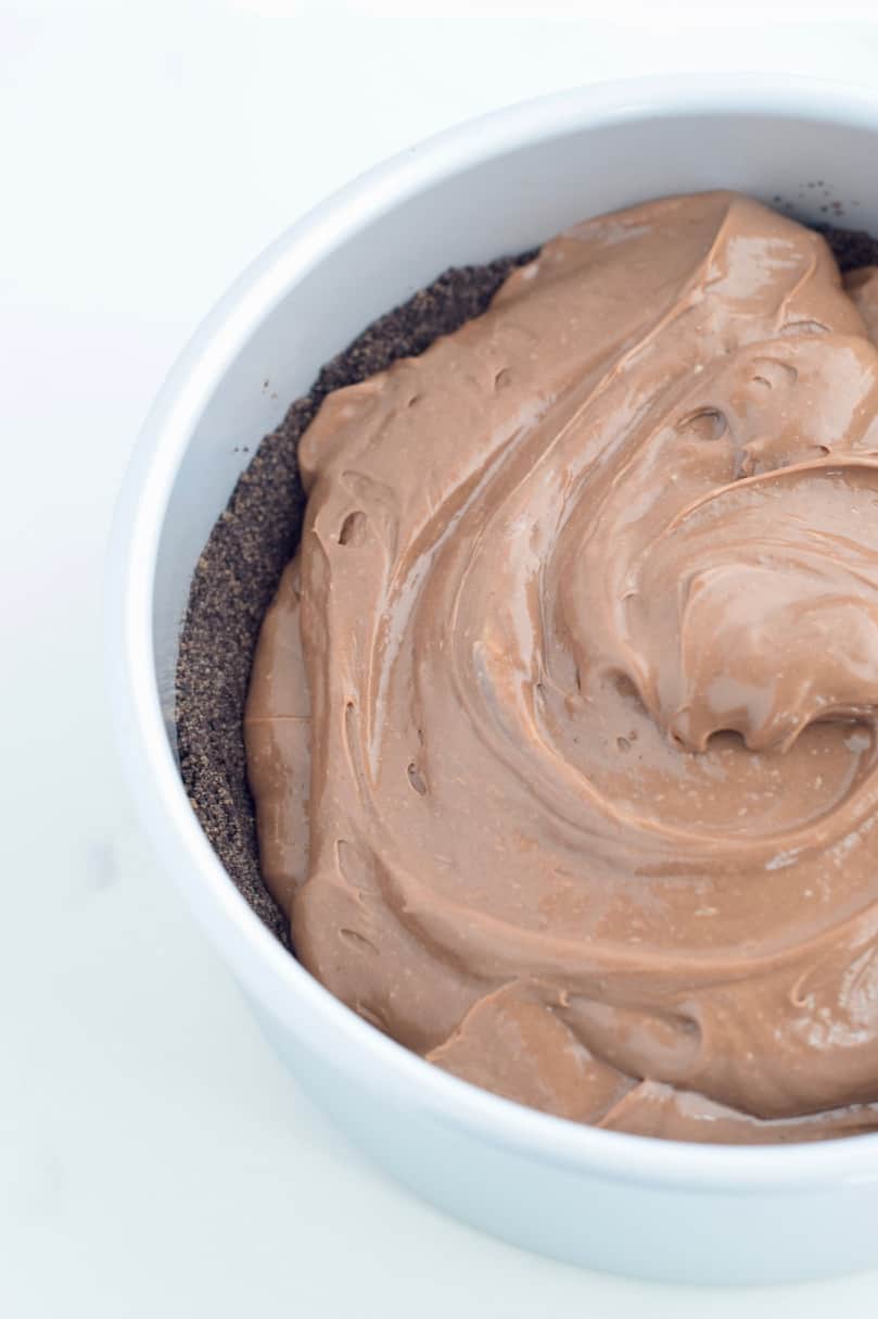 chocolate cheesecake batter dolloped on chocolate crumb crust in a cake pan