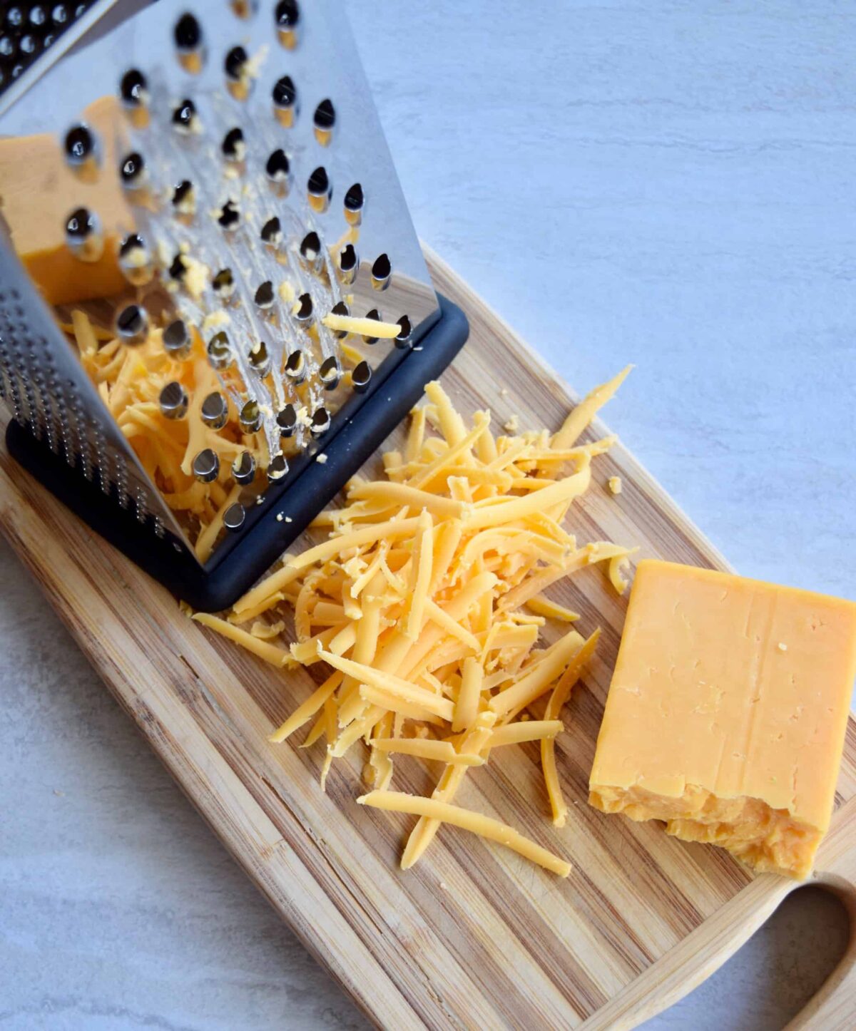 cheese grater with shredded cheddar on a cutting board