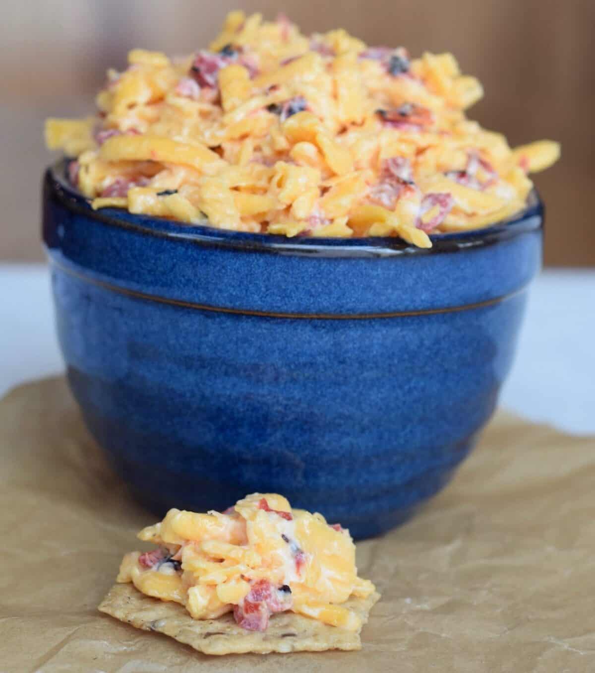 pimento cheese in blue crock with some on a cracker on parchment paper