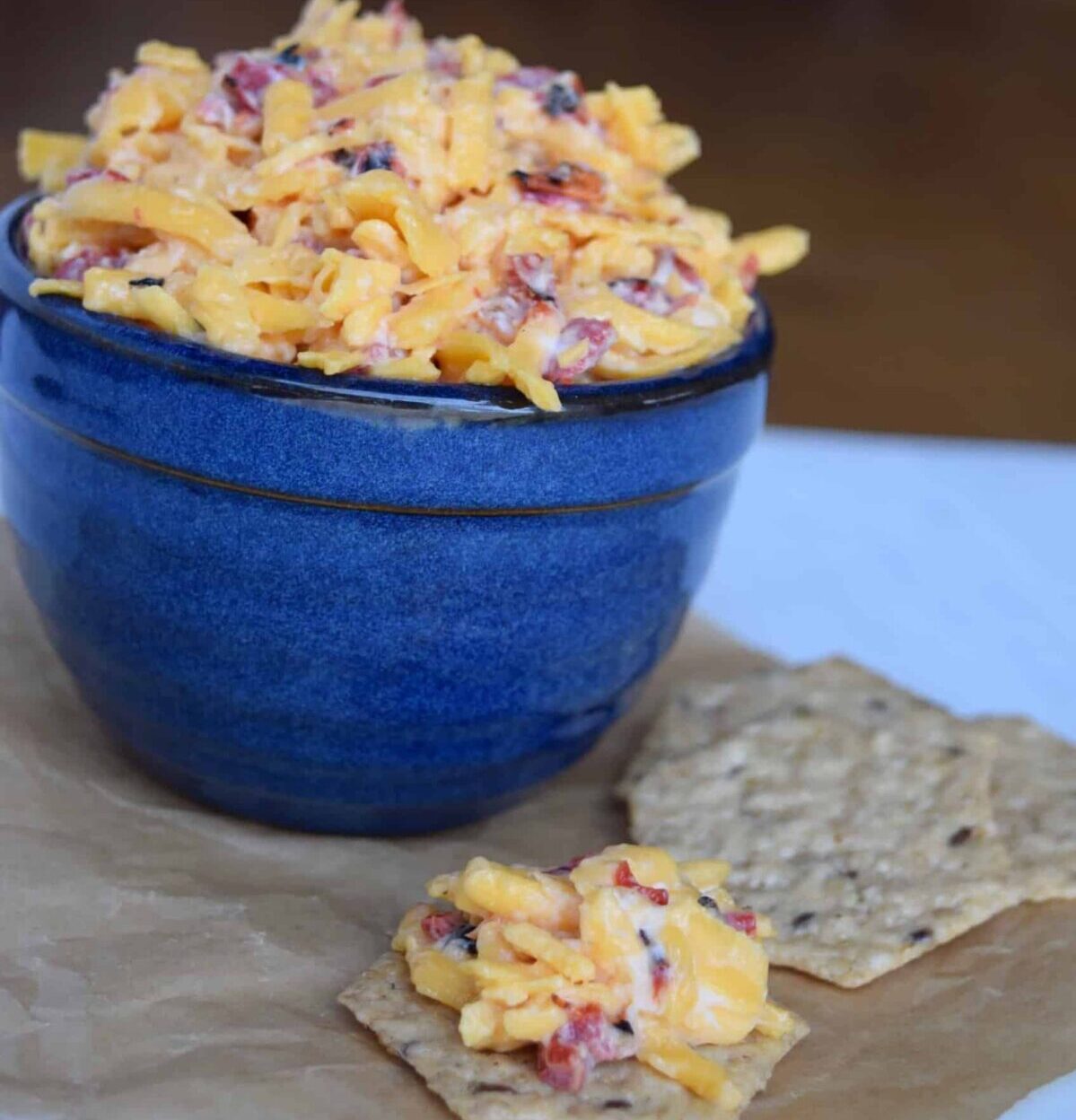 pimento cheese in a blue crock with some on a cracker on brown parchment