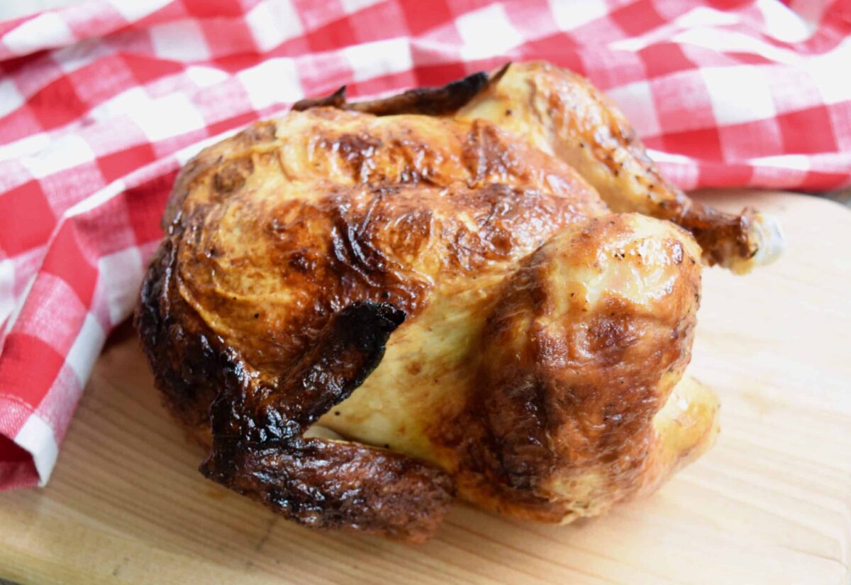 rotisserie chicken on wooden surface next to red white checked cloth