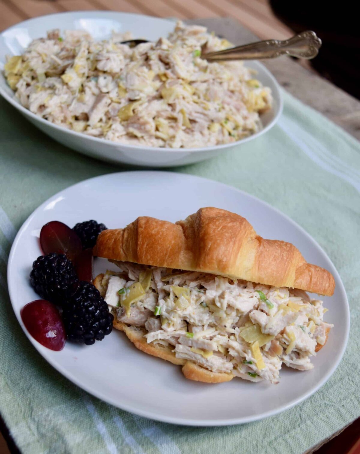 chicken salad in a croissant with blackberries and red grapes beside it