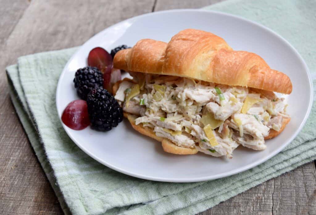 Parmesan Artichoke chicken salad on a croissant on a white plate 