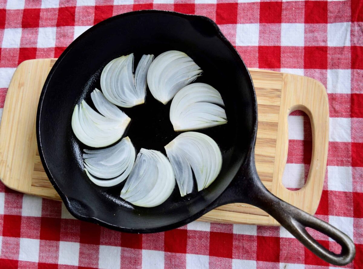 vidalia onion fans in bottom of cast iron skillet on a wooden cutting board on a red checked cloth