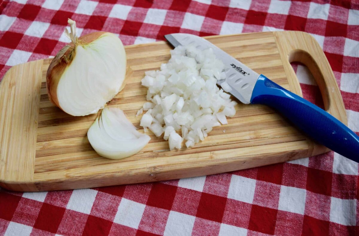 half an onion on a wooden cutting board on a red checked table cloth. The other half of onion is chopped and sliced