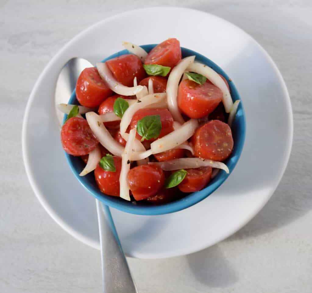tomato onion salad in a blue bowl sitting in a white bowl with a spoon to the side