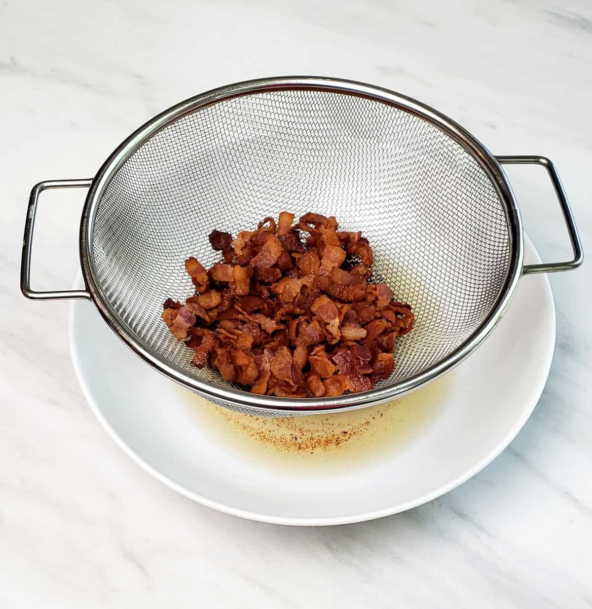 Drained chopped cooked bacon in a metal sieve