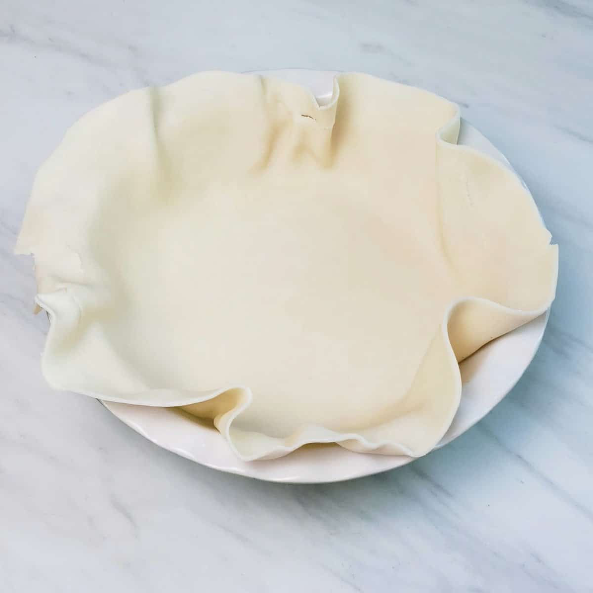 Pillsbury pie crust unrolled and laid in a white pie dish on marble surface