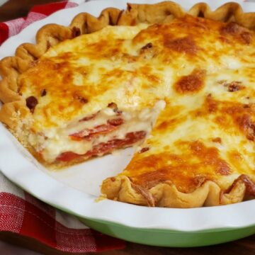 Tomatoes and onion pie layered with slice out in a fluted white and green pie dish