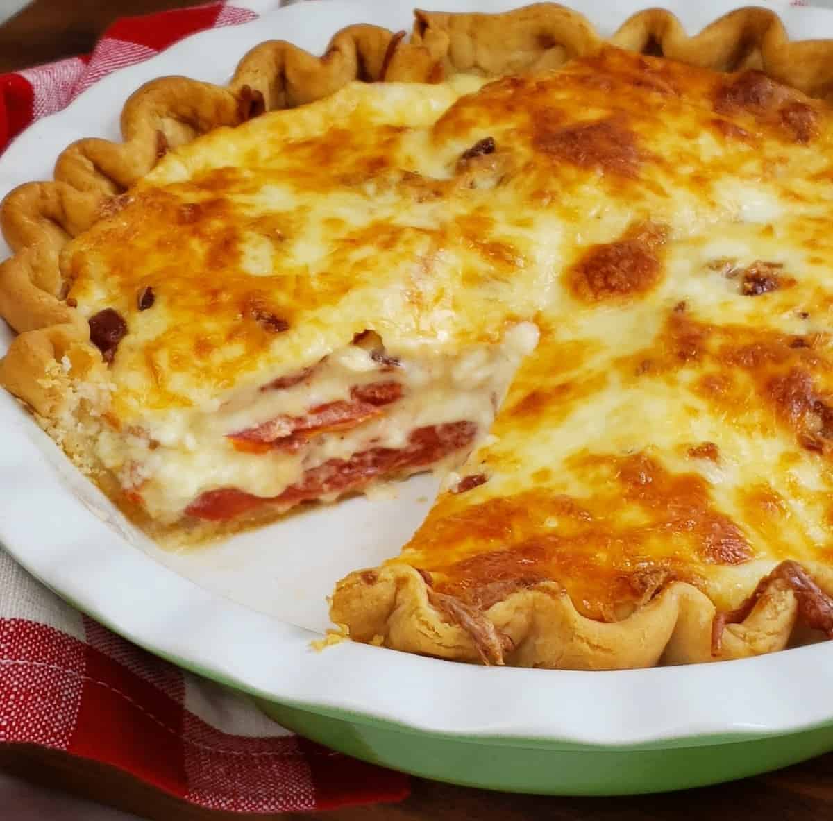 Tomatoes and onion pie layered with slice out in a fluted white and green pie dish