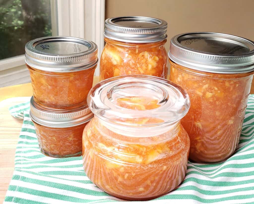 5 jars of various sizes of Peach Freezer Marmalade on a green striped tea towel