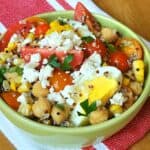 Tri color quinoa salad with grape tomatoes boiled egg and chick peas in a green bowl on a red and white napkin with feta