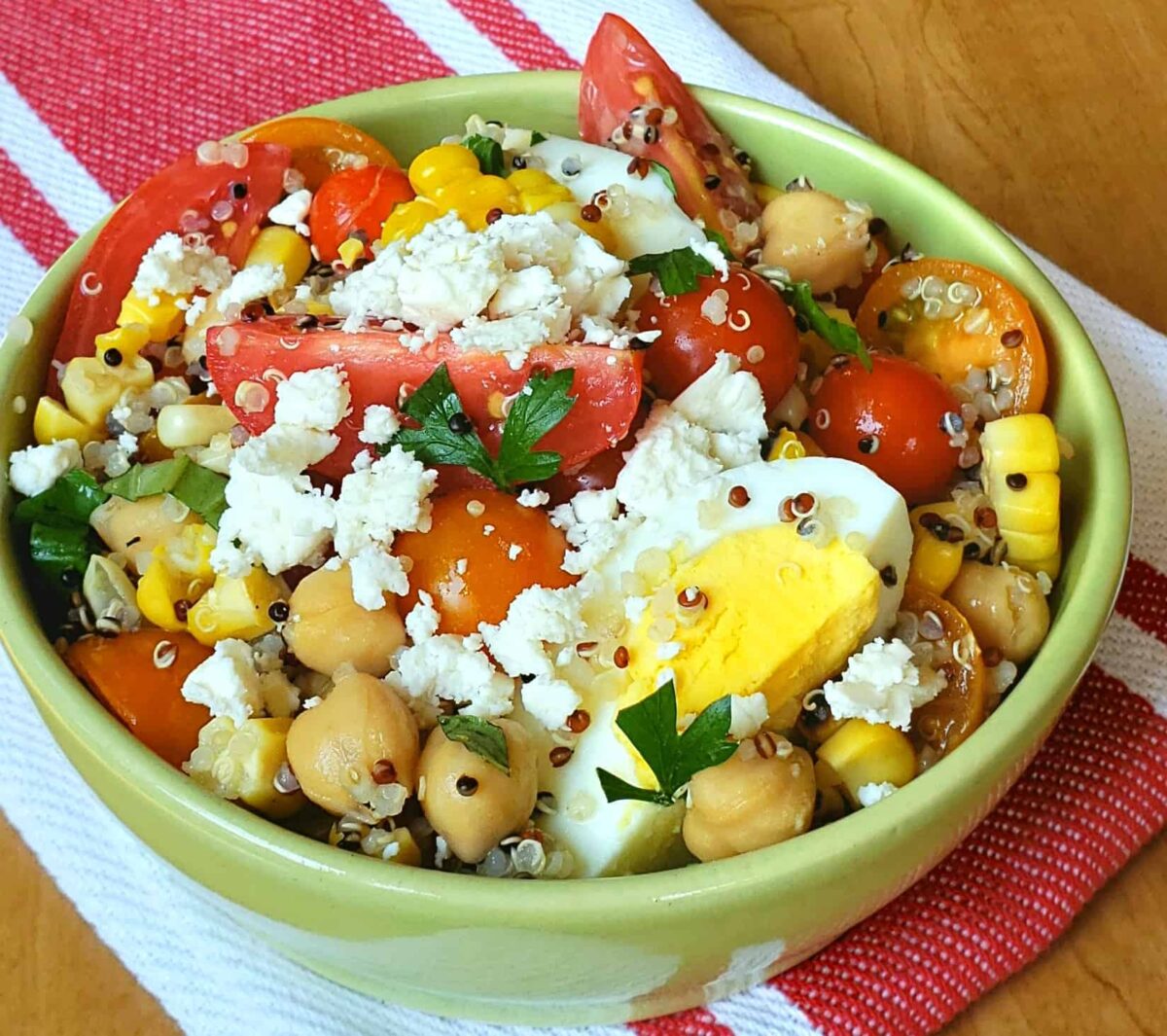 Tri Color Quinoa Salad is packed with protein and bursting with color and flavor. quinoa salad with grape tomatoes boiled egg and chick peas in a green bowl on a red and white napkin with feta