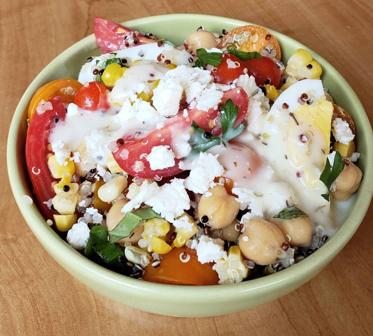 Tri color quinoa salad with grape tomatoes boiled egg and chick peas in a green bowl on a red and white napkin with Greek dressing