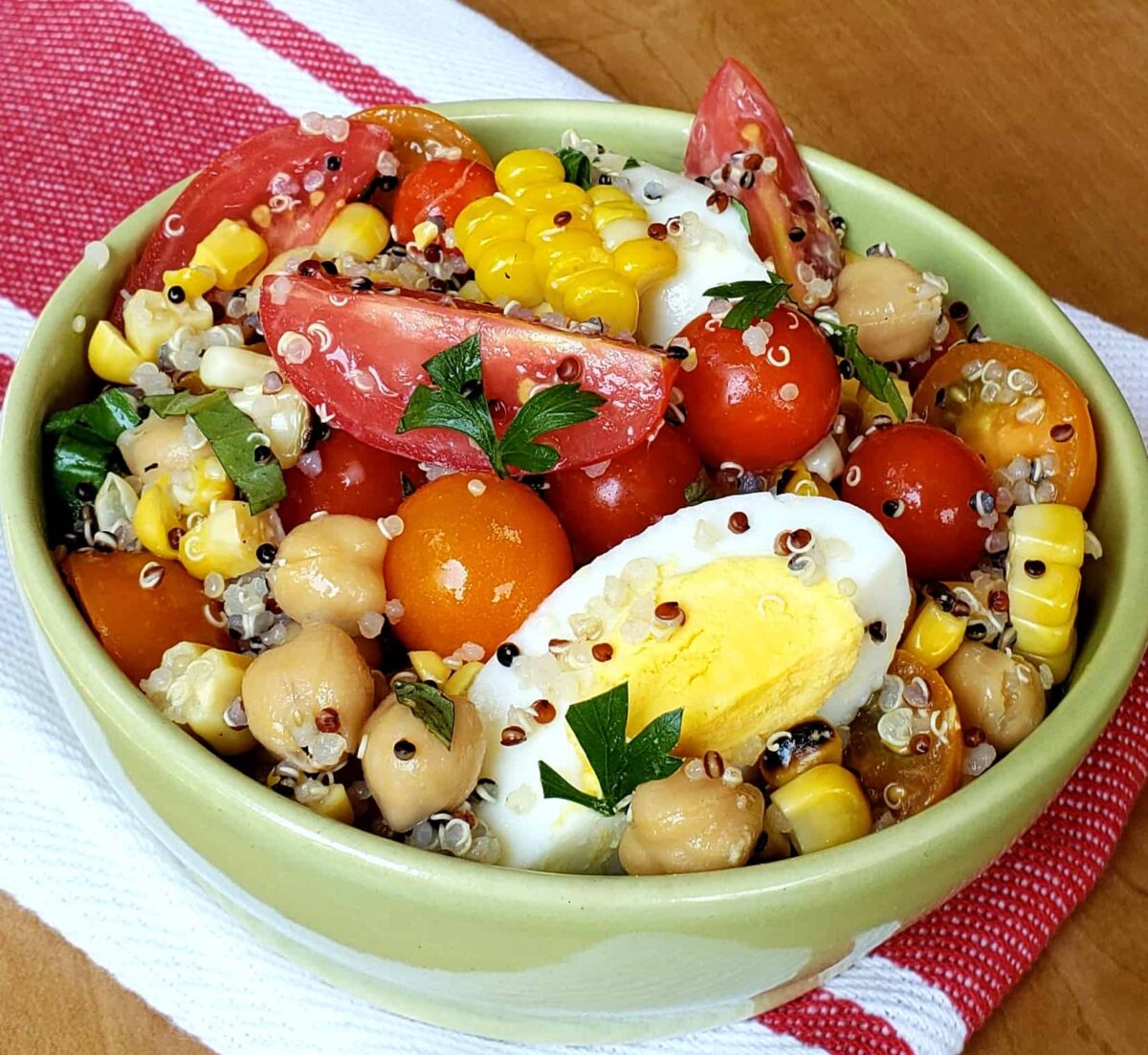 Tri color quinoa salad with grape tomatoes boiled egg and chick peas in a green bowl on a red and white napkin