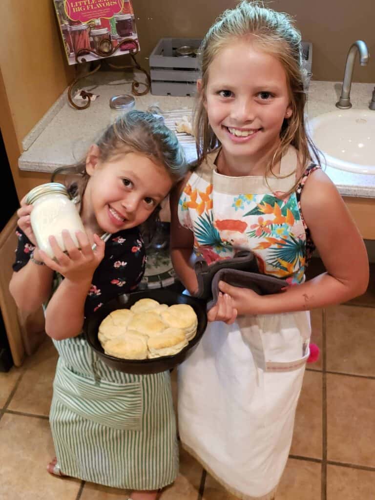 Two girls holding a cast iron skillet of biscuits and a jar of homemade butter
