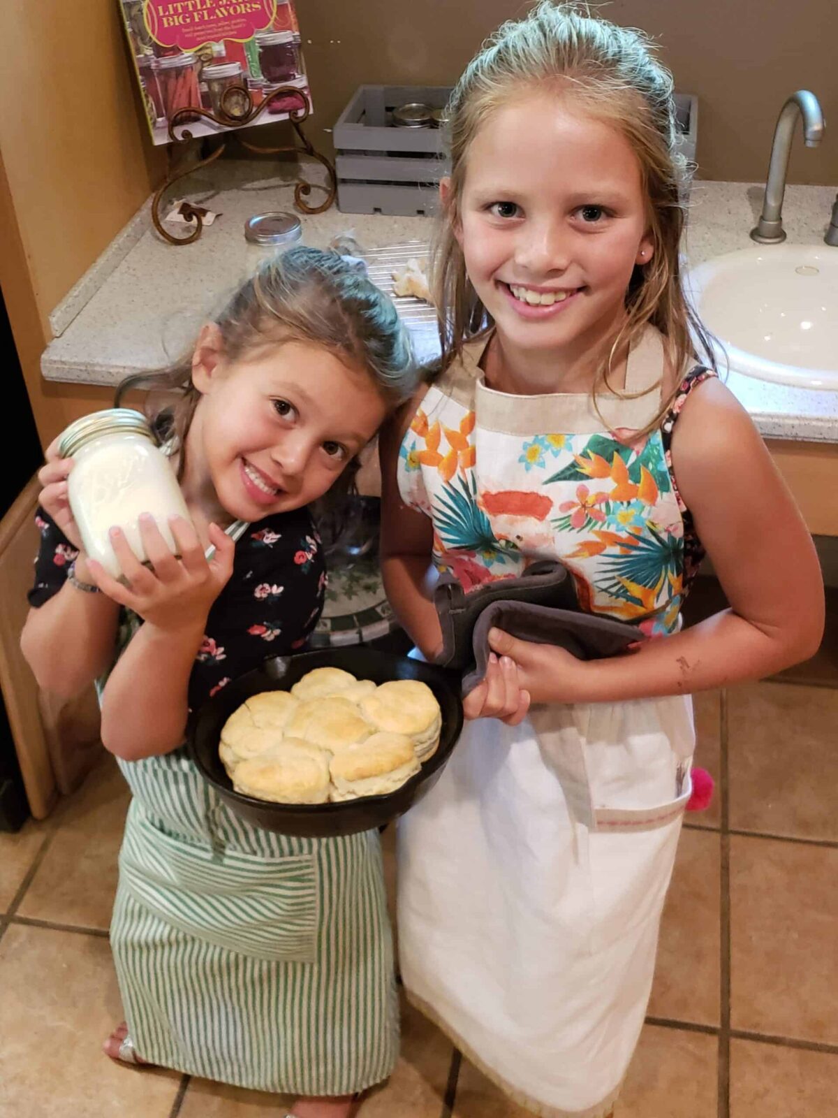 two girls holding cast iron skillet full of biscuits and a jar of homemade butter