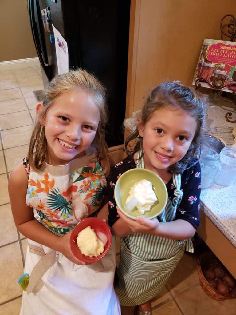 Two girls in aprons holding bowls of homemade butter