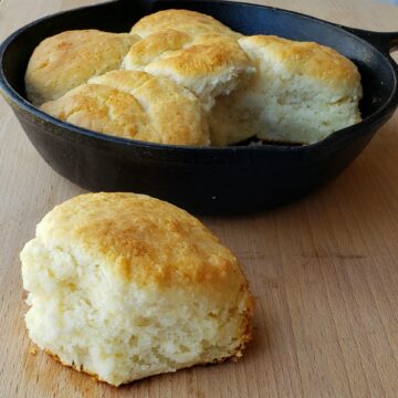 small cast iron skillet with biscuits; one biscuit on wooden surface