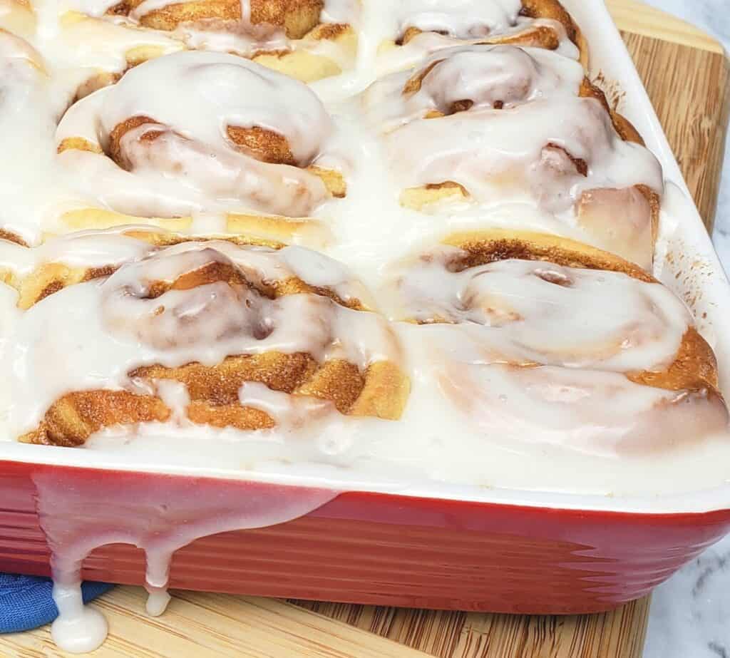 Cinnamon rolls in red baking dish with icing drip