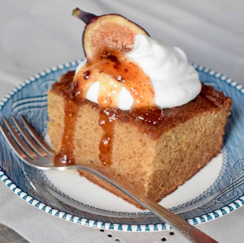 Square piece of fig cake topped with dollop whipped cream, jam and a fig half