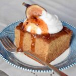 Square piece of Fig Jam Cake topped with dollop whipped cream, Fig and Lemon Preserves and a fig half