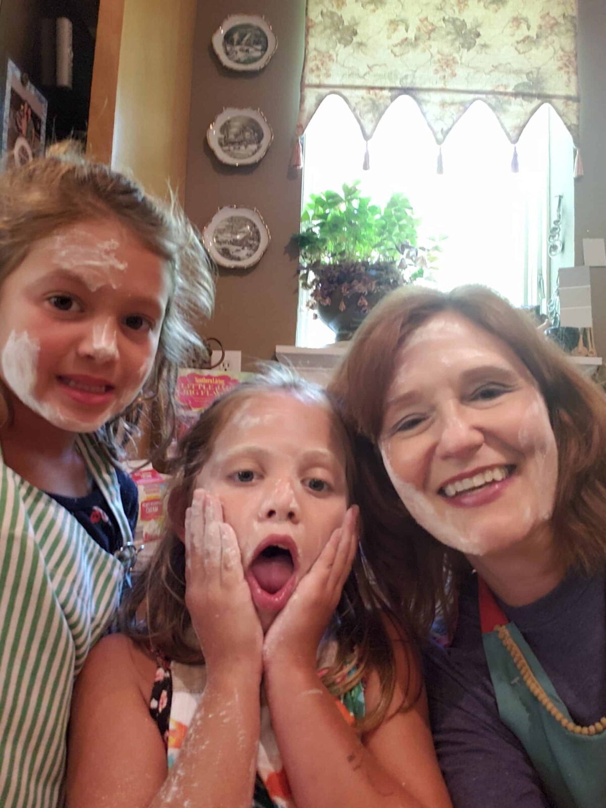 Kathleen Phillips with two girls helping in the kitchen with flour on their faces.