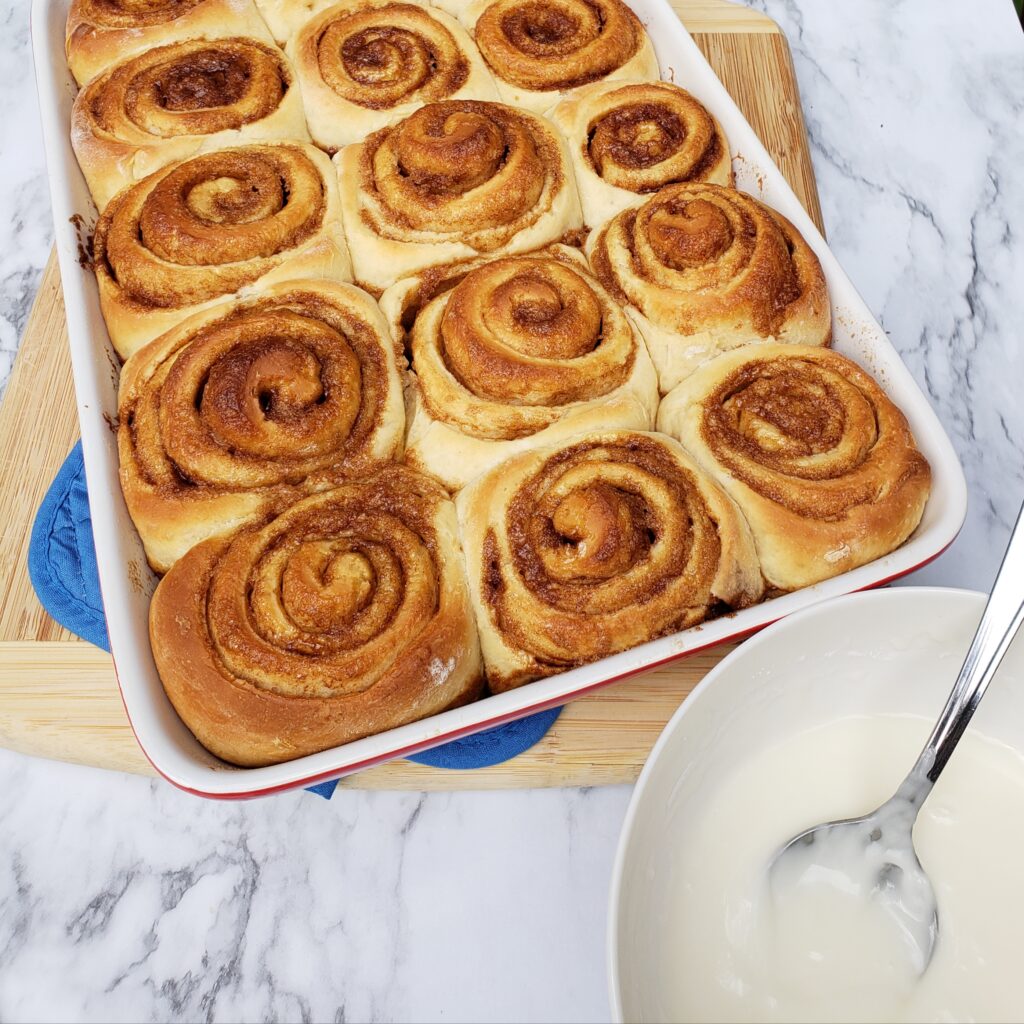 unbaked cinnamon rolls with bowl of icing