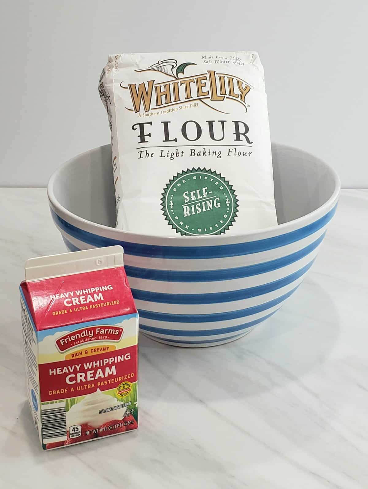 a bag of White Lily flour in a blue striped bowl with a quart of heavy whipping cream next to it